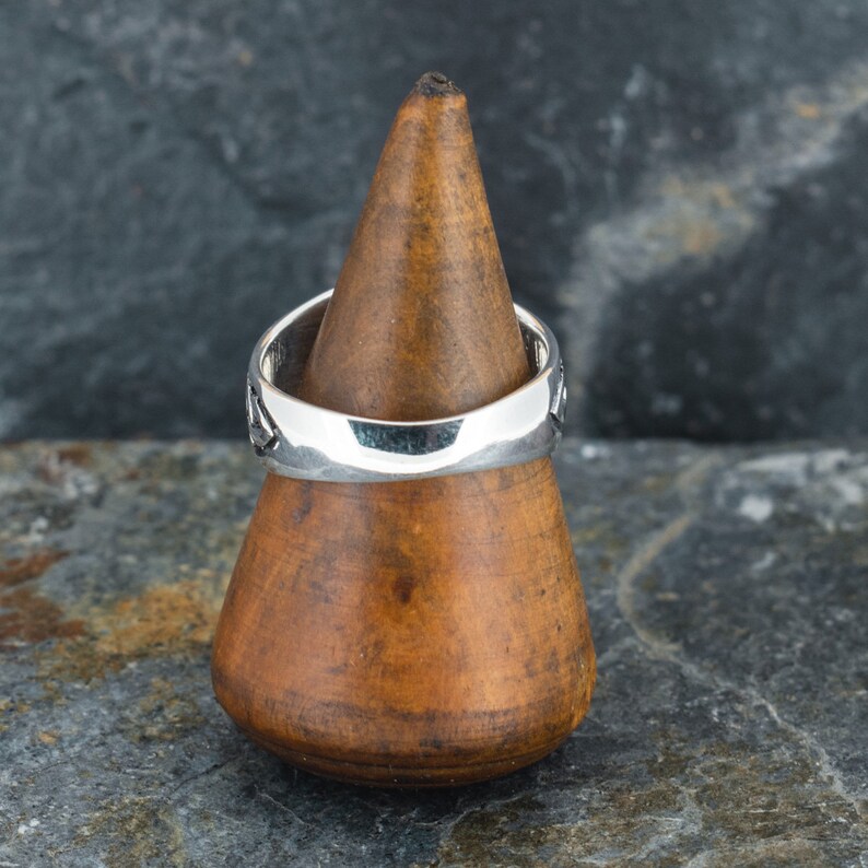 May include: A silver ring with a textured design, displayed on a wooden ring holder.