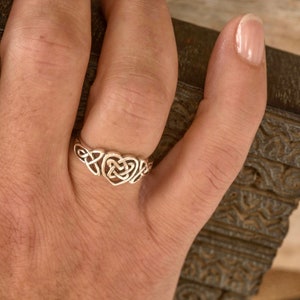 May include: A silver ring featuring a Celtic knot heart design. The ring is worn on a finger, showcasing the intricate openwork pattern. The ring's design is a symbol of love and eternity.