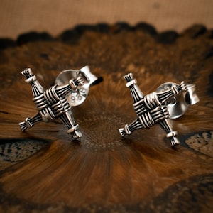 May include: A pair of silver Celtic knot earrings. The earrings are in the shape of a cross with a woven design.