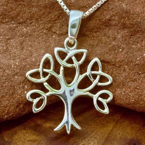 Puede incluir: Un collar con un colgante de plata en forma de árbol de la vida celta. El colgante presenta un árbol estilizado con ramas y hojas hechas de nudos entrelazados. El collar es un símbolo popular de fuerza, crecimiento y conexión.