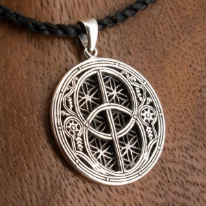 May include: Silver pendant necklace with a circular design featuring intricate Celtic knotwork and a central symbol. The pendant is suspended from a black cord.