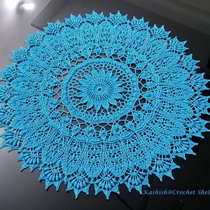 Puede incluir: Un gran encaje de ganchillo redondo de color azul turquesa brillante. El encaje tiene un diseño delicado e intrincado con un motivo floral central.