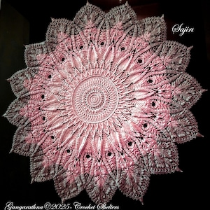 Puede incluir: Un gran encaje de ganchillo intrincado en tonos de rosa y blanco. El encaje tiene un diseño circular con un motivo central y radios que irradian hacia afuera. El encaje está hecho con puntadas delicadas y tiene un aspecto de encaje. El texto "Sajiira" es visible en la esquina superior derecha de la imagen. El texto "Gangarathna ©2023 - Crochet Shelters" es visible en la esquina inferior izquierda de la imagen.