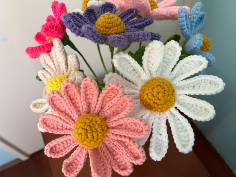 Op de afbeelding: Een boeket van gehaakte bloemen in verschillende kleuren, waaronder roze, wit, paars, blauw en geel. De bloemen zijn in een vaas gerangschikt en hebben een realistisch uiterlijk.