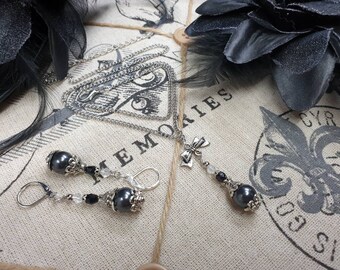 May include: A silver chain necklace with a black pearl pendant and a silver bow charm. Matching earrings with black pearls and silver accents.