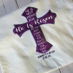 以下が含まれることがあります： パープルグリッター刺繍の十字架に「He Is Risen」の文字とマタイによる福音書28章6節の聖句が書かれています。