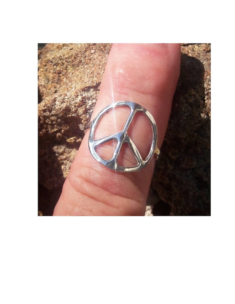 K&ouml;nnte beinhalten: Ein silberner Friedenszeichenring, der an einem Finger getragen wird.
