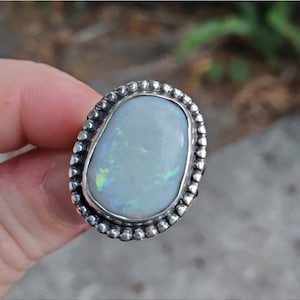 May include: A silver ring with a white opal gemstone set in a beaded bezel.