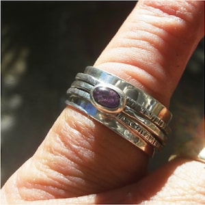May include: A silver ring with three bands and a purple gemstone. The ring is worn on a finger.