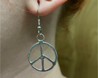 May include: Silver peace sign earrings with a simple design. The earrings are hanging from a person's ear.