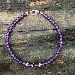 May include: A purple amethyst beaded bracelet with silver accents. The bracelet is made with small round beads and has a silver clasp.