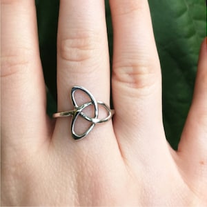 May include: A silver ring with a Celtic knot design. The ring is worn on a finger.