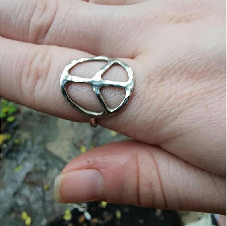 K&ouml;nnte beinhalten: Ein silberner Peace-Zeichen-Ring mit geh&auml;mmerter Textur. Der Ring wird an einem Finger getragen.