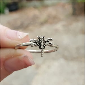 May include: A silver ring featuring a dragonfly design. The dragonfly is detailed with textured wings and a segmented body.
