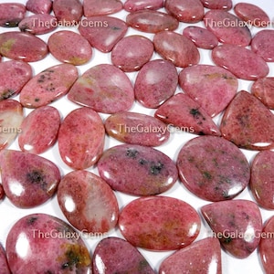 May include: A collection of pink and white gemstone cabochons. The cabochons are oval and teardrop shaped and have a smooth, polished finish.