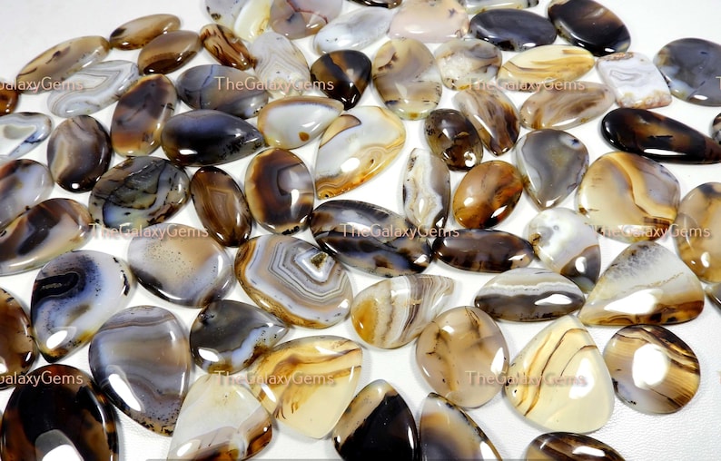 May include: A collection of agate cabochons in various shades of brown, white, and gray. The cabochons are smooth and polished, with intricate patterns and swirls.