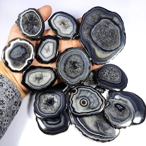 May include: A collection of polished agate slices in various sizes and shapes. The stones feature concentric bands of gray, black, and white, creating unique patterns. These decorative stones are ideal for home decor or crafting projects.