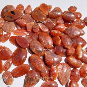 May include: A collection of approximately 40 sunstone cabochons in various shapes and sizes. The stones are a mix of orange, red, and brown with a shimmery, iridescent quality.