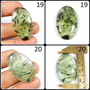 May include: Two oval-shaped green and black gemstone cabochons, one is being measured with a ruler, the other is being held in a hand. The ruler shows measurements in inches. The cabochons are approximately 1 inch in length.