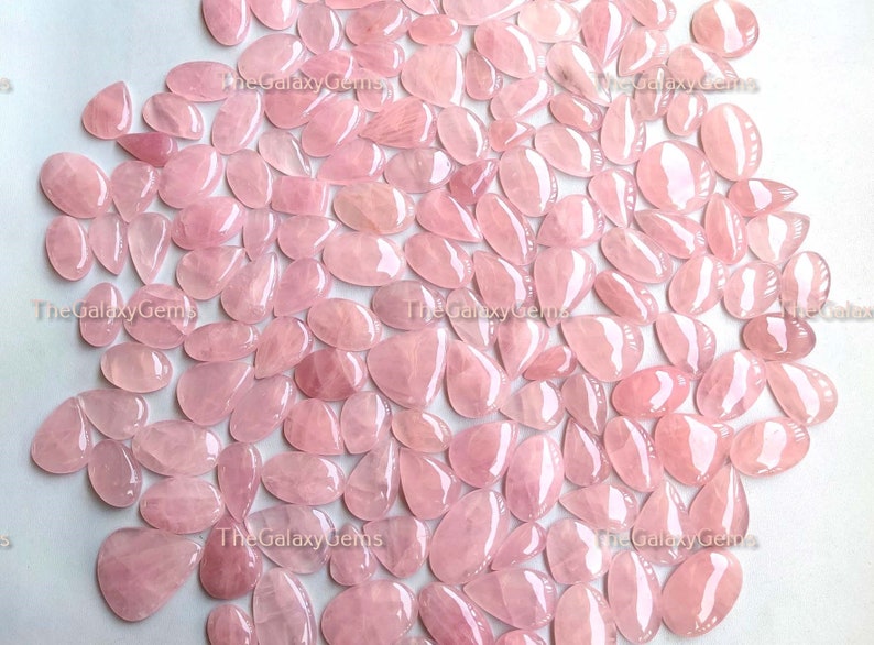 May include: A large group of pink rose quartz cabochons in a teardrop shape. The stones are smooth and polished, with a translucent appearance.