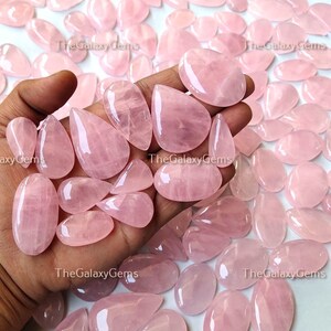May include: A collection of pink rose quartz cabochons, some with a teardrop shape, others with a more oval shape. The stones are smooth and polished, with a translucent appearance.