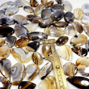 May include: A collection of agate cabochons in various shades of brown, white, and gray. The cabochons are oval-shaped and have a smooth, polished finish. The cabochons are arranged in a random pattern on a white surface.