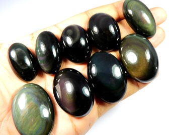 May include: A collection of polished, oval-shaped obsidian gemstones. The stones vary in size and display iridescent swirls of green, gold, and purple within a predominantly black surface. The gemstones are held in a hand.
