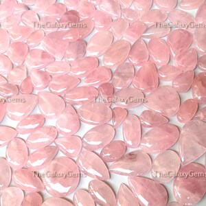 May include: A large collection of pink rose quartz cabochons, all in various shapes and sizes. The stones are smooth and polished, with a translucent appearance.