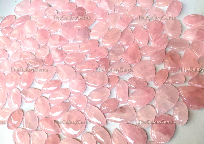 May include: A large collection of pink rose quartz cabochons, all in various shapes and sizes. The stones are smooth and polished, with a translucent appearance.