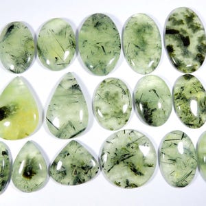 May include: A collection of 15 green and black gemstone cabochons. The cabochons are oval and pear shaped. They have a translucent appearance with a variety of green and black inclusions.