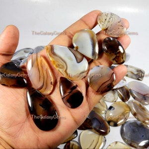 May include: Assortment of agate cabochons in various shades of brown, white, and gray. The cabochons are teardrop and oval shaped, with intricate banding patterns.