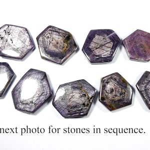 Puede incluir: Diez piedras preciosas hexagonales, de color púrpura oscuro, con brillo metálico, dispuestas sobre una superficie blanca. Las piedras tienen un patrón en forma de estrella y son de diferentes tamaños. El texto en la parte inferior dice: "Ver la siguiente foto para ver las piedras en secuencia".