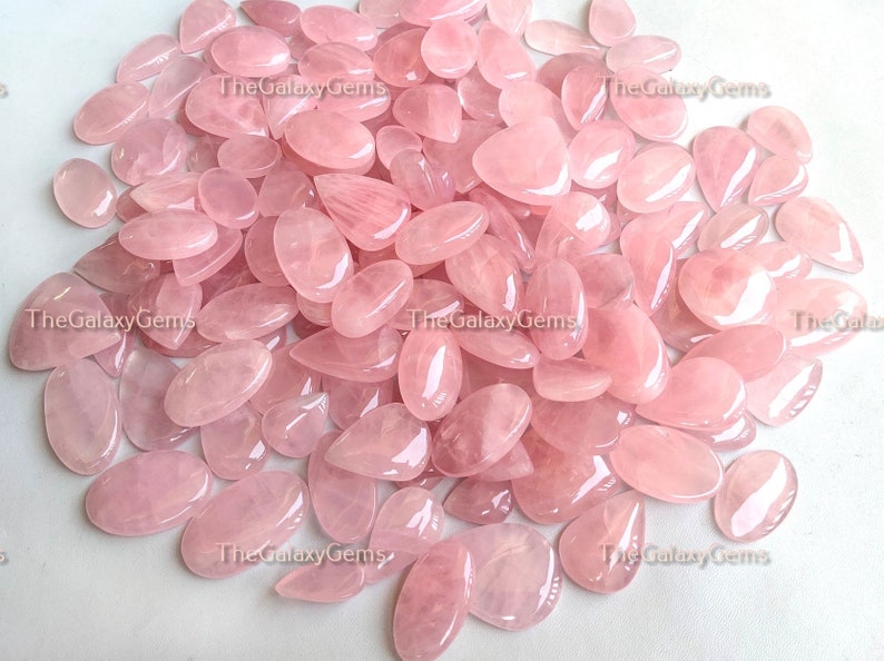 May include: A large pile of pink rose quartz gemstone cabochons in various sizes and shapes. The stones are smooth and polished, with a translucent appearance.