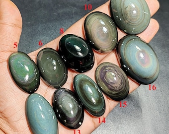 May include: A collection of polished oval rainbow obsidian gemstones labeled with red numbers 5, 6, 8, 10, 11, 12, 13, 14, 15, and 16. Each stone displays unique concentric bands of iridescent green, purple, and gold hues against a dark base.