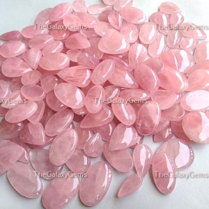 May include: A large pile of pink rose quartz gemstones, all cut into a teardrop shape. The stones are smooth and polished, with a translucent appearance.