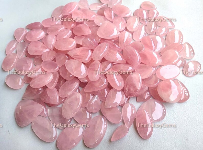 May include: A large pile of pink rose quartz gemstones, all cut into a teardrop shape. The stones are smooth and polished, with a translucent appearance.