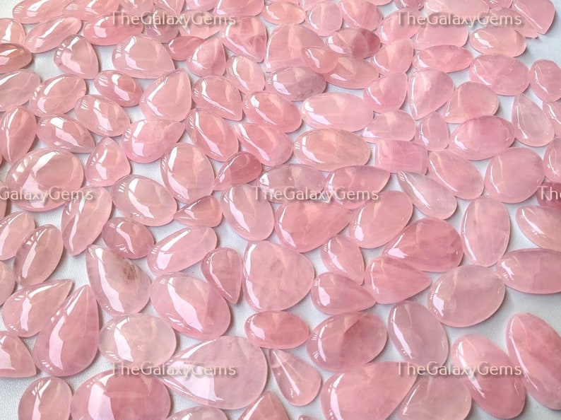 May include: A collection of pink rose quartz cabochons, each with a smooth, polished surface. The stones are various sizes and shapes, with a translucent, light pink color.