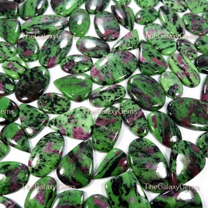 May include: A collection of green, pink, and black gemstone cabochons. The stones are oval shaped and have a smooth, polished finish.