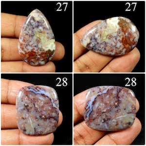 May include: Four polished cabochons of patterned agate stone. Two teardrop-shaped stones labelled 27 feature swirling red, brown, and white inclusions. Two rectangular stones labelled 28 display a mottled mix of purple, red, and white mineral patterns.
