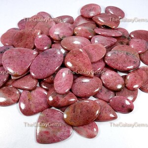 May include: A collection of pink and red gemstone cabochons, with a smooth, polished finish. The stones are oval and teardrop shaped, and have a natural, organic look.