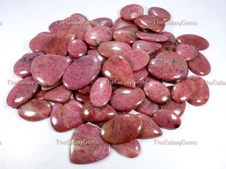 May include: A collection of pink and red gemstone cabochons, with a smooth, polished finish. The stones are oval and teardrop shaped, and have a natural, organic look.