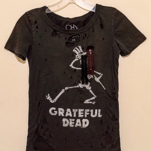 May include: Distressed dark green t-shirt featuring a white skeleton graphic playing a guitar and the text "Grateful Dead".