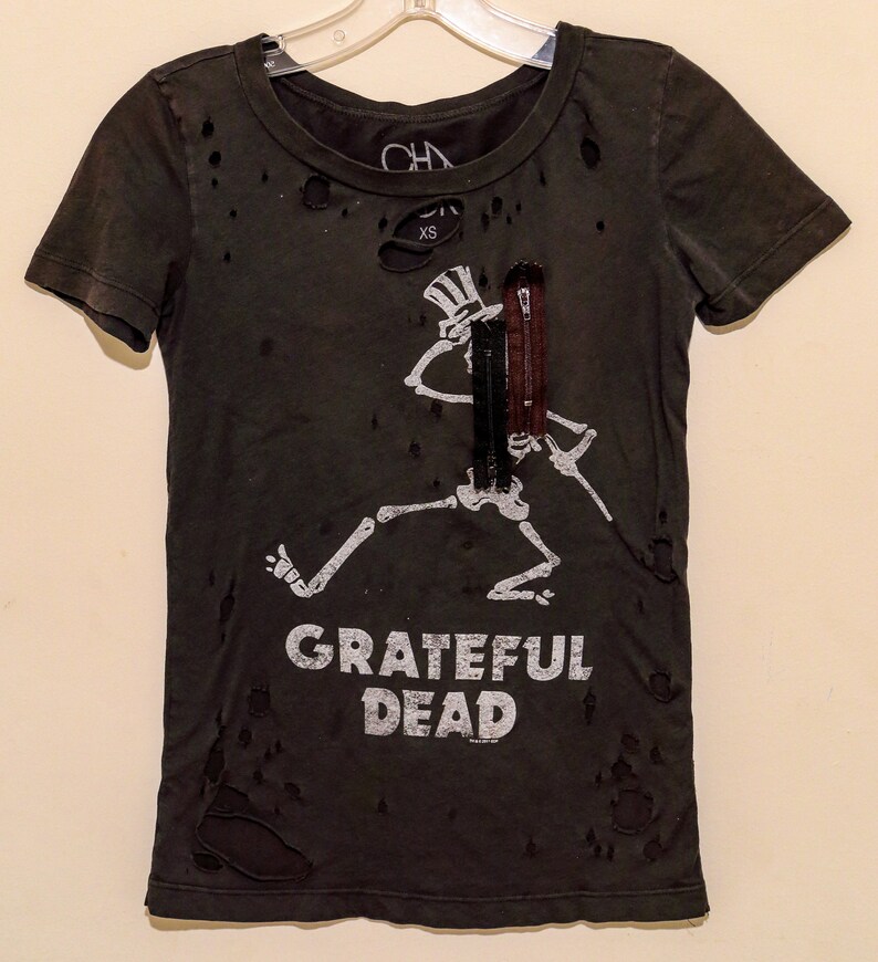 May include: Distressed dark green t-shirt featuring a white skeleton graphic playing a guitar and the text "Grateful Dead".