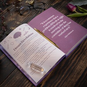 May include: Open book with purple pages and a gold pen on top. The book is titled "Dream Revelations" and has a quote from John Steinbeck about dreams. The quote reads: "It is a common experience that a problem difficult at night is resolved in the morning after the committee of sleep has worked on it."