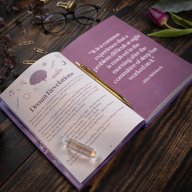 May include: Open book with purple pages and a gold pen on top. The book is titled "Dream Revelations" and has a quote from John Steinbeck about dreams. The quote reads: "It is a common experience that a problem difficult at night is resolved in the morning after the committee of sleep has worked on it."