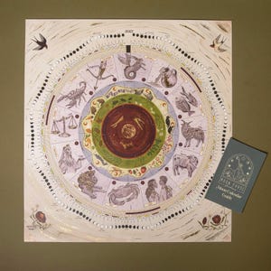 May include: A 2027 circular wall calendar featuring zodiac signs, moon phases, and seasonal illustrations in earthy tones. The design includes a central sun, surrounding astrological figures, and a separate blue Moon Calendar Guide booklet.