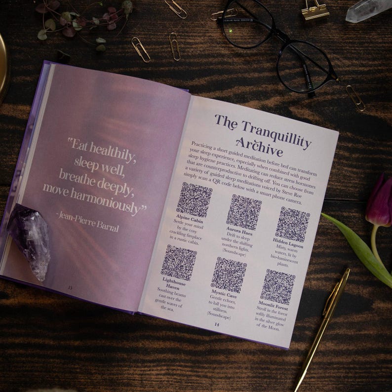 May include: An open book with a purple cover and a quote about health and well-being. The book features a section titled "The Tranquillity Archive" with QR codes for guided meditations. The quote reads "Eat healthily, sleep well, breathe deeply, move harmoniously" - Jean-Pierre Barral.
