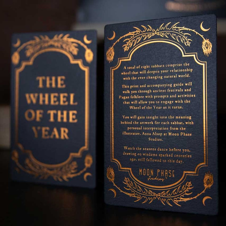 May include: A black card with gold lettering that reads "The Wheel of the Year". The card is part of a set of cards that explore the eight sabbats of the Wheel of the Year. The card is illustrated with a stylized floral design.