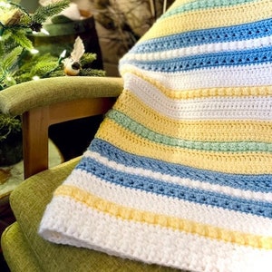 May include: A white, yellow, blue and green striped crocheted blanket draped over a wooden chair with a green cushion.