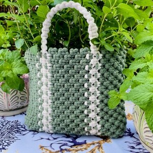 May include: A green and white crocheted tote bag with a thick rope handle. The bag is sitting on a blue and white patterned surface.
